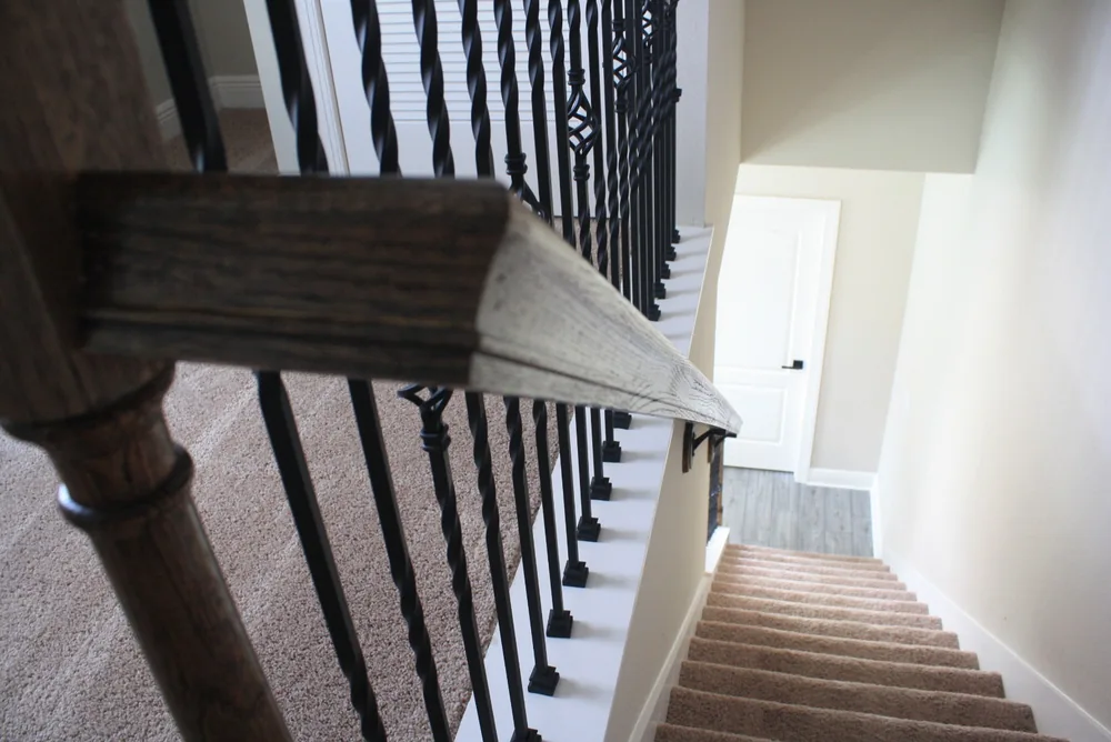 Detalle de pasamanos teñido con balaustres de metal negro sobre una escalera alfombrada